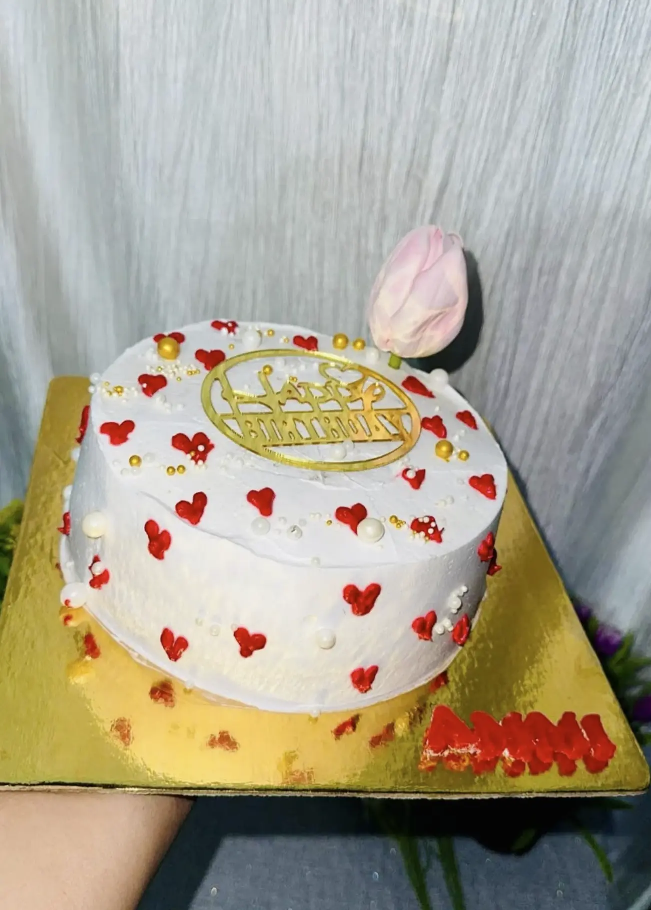 White frosted cake with red hearts, gold pearls and a pink tulip by Kaur Bakehouse